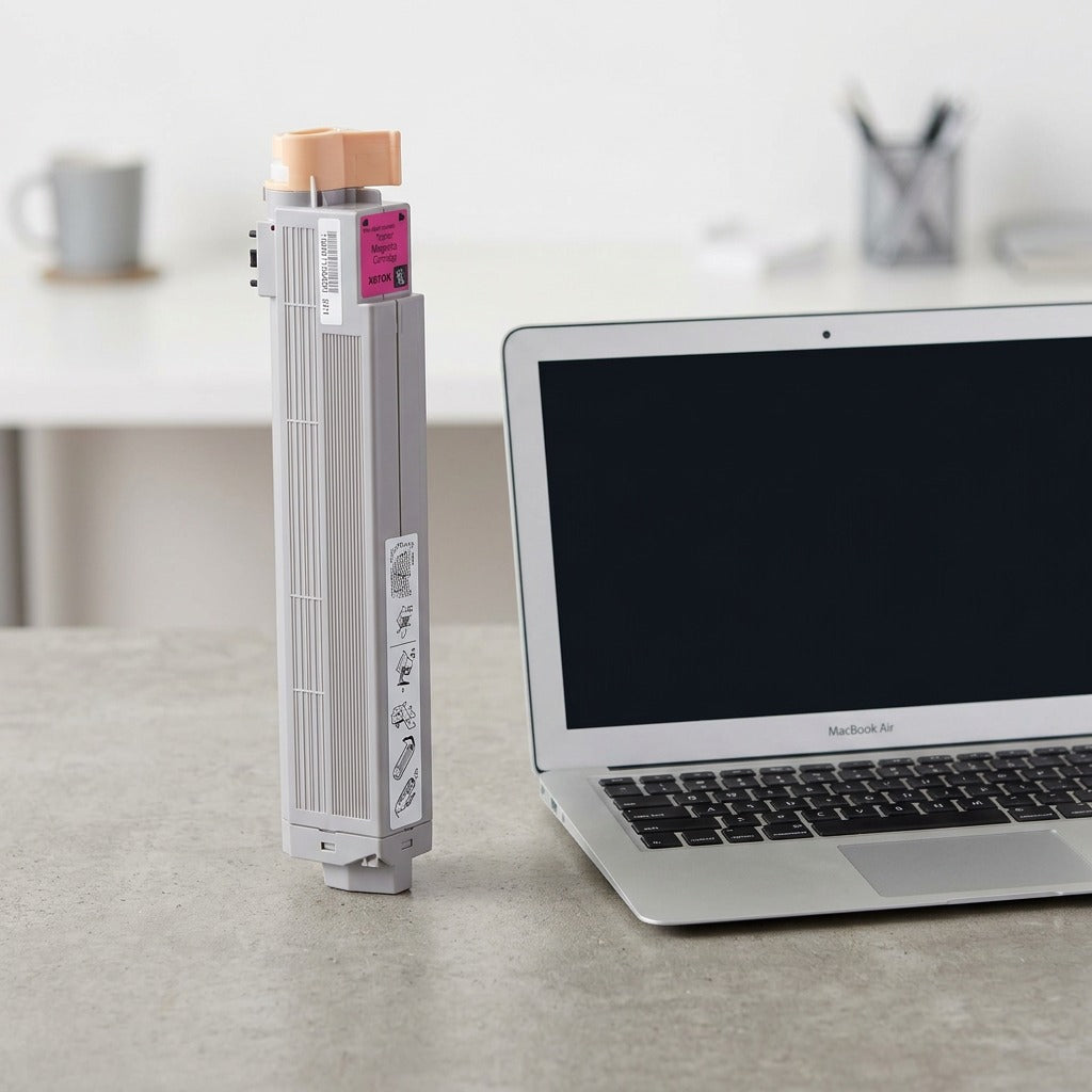 A photograph in a home office setting of the grey Xerox 106R01078 toner cartridge standing upright next to an open, average-sized laptop.