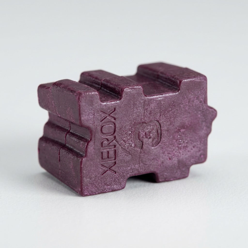 Macro shot of a magenta solid ink stick showing the Xerox logo on its waxy surface texture.
