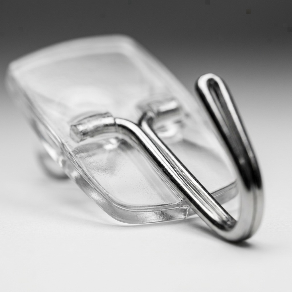 Extreme macro view showcasing the polished metal hook and the crystal-clear adhesive strip of a single Command Clear Small Wire Hook.