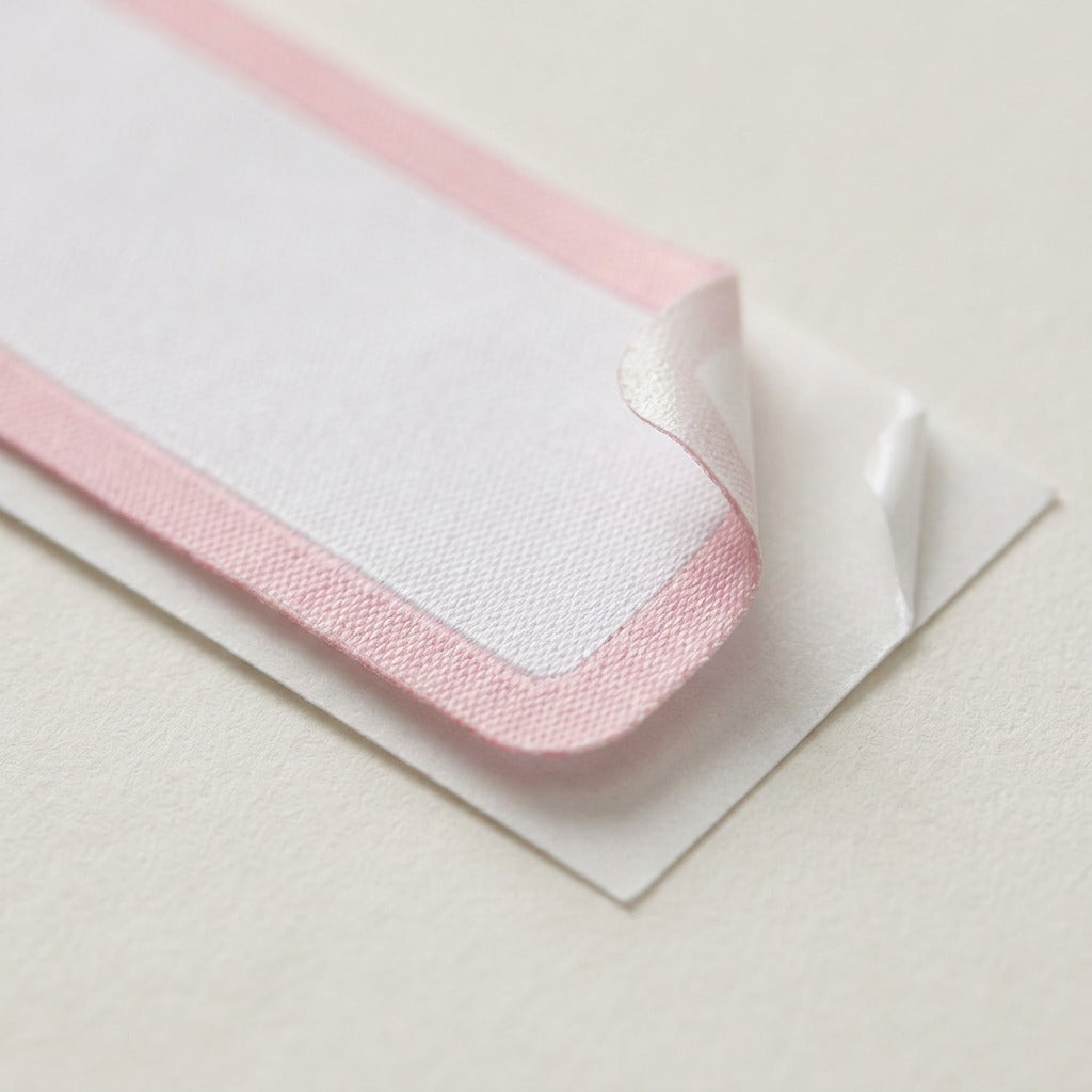 Extreme close-up of an Avery No-Iron label, showing detailed fabric weave, pink border, and adhesive-coated underside.
